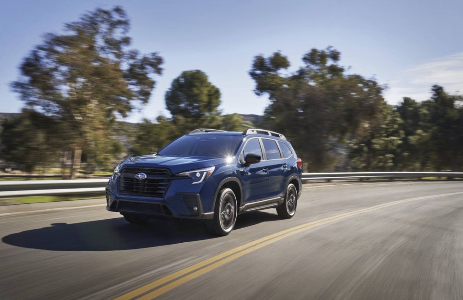 2026 Subaru Ascent in blue driving a tree-lined road, front three-quarter view