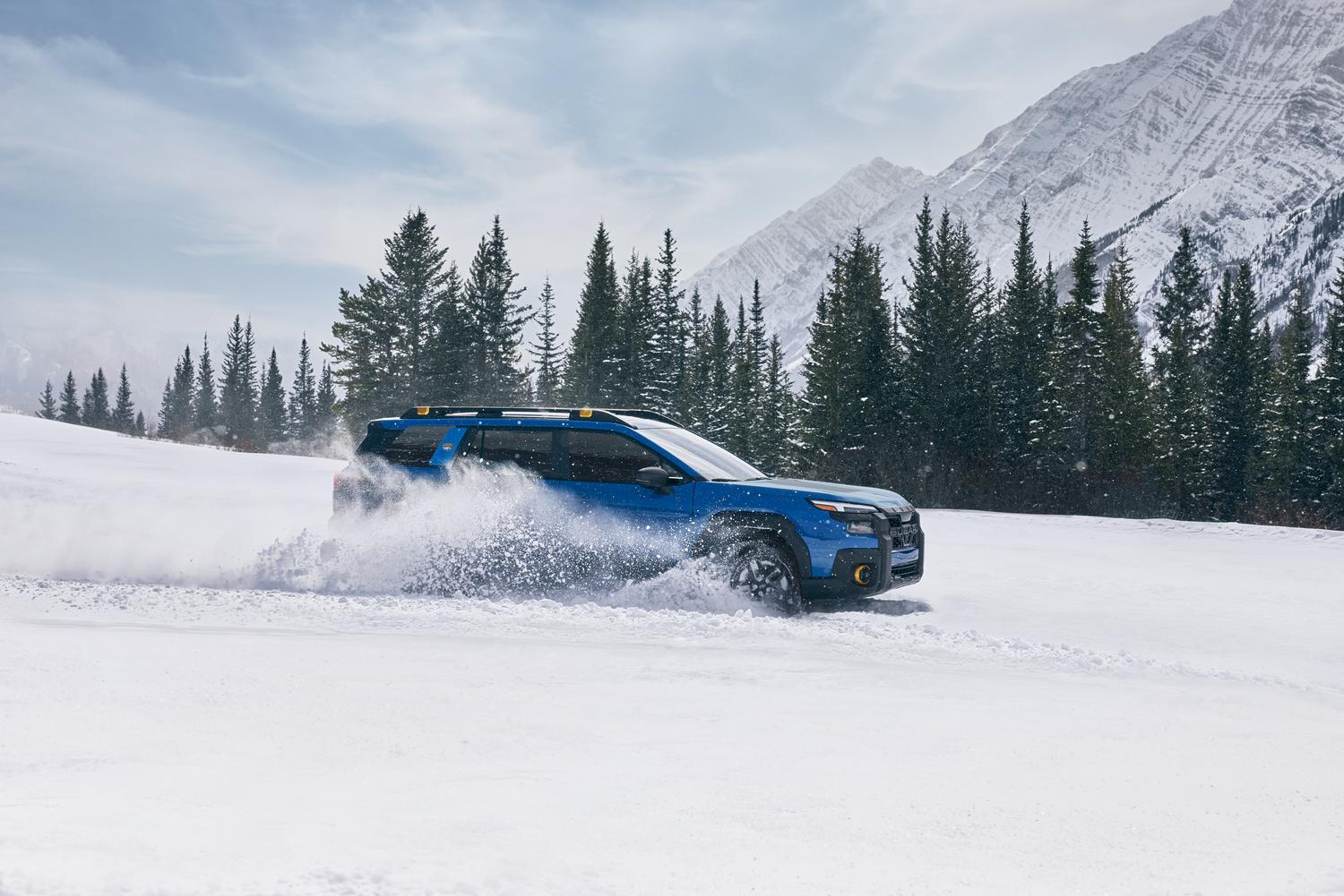 2026 Subaru Outback in blue driving through deep snow with mountains behind